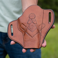 Person holding a brown leather gun holster with Masonic emblem outdoors